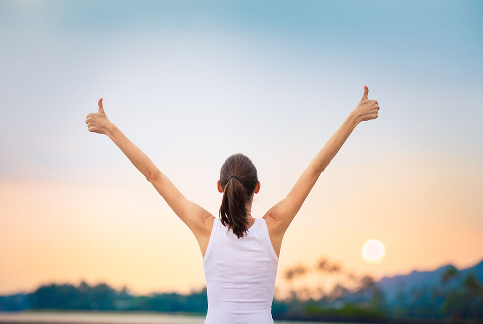 Confident woman giving thumbs up at sunrise