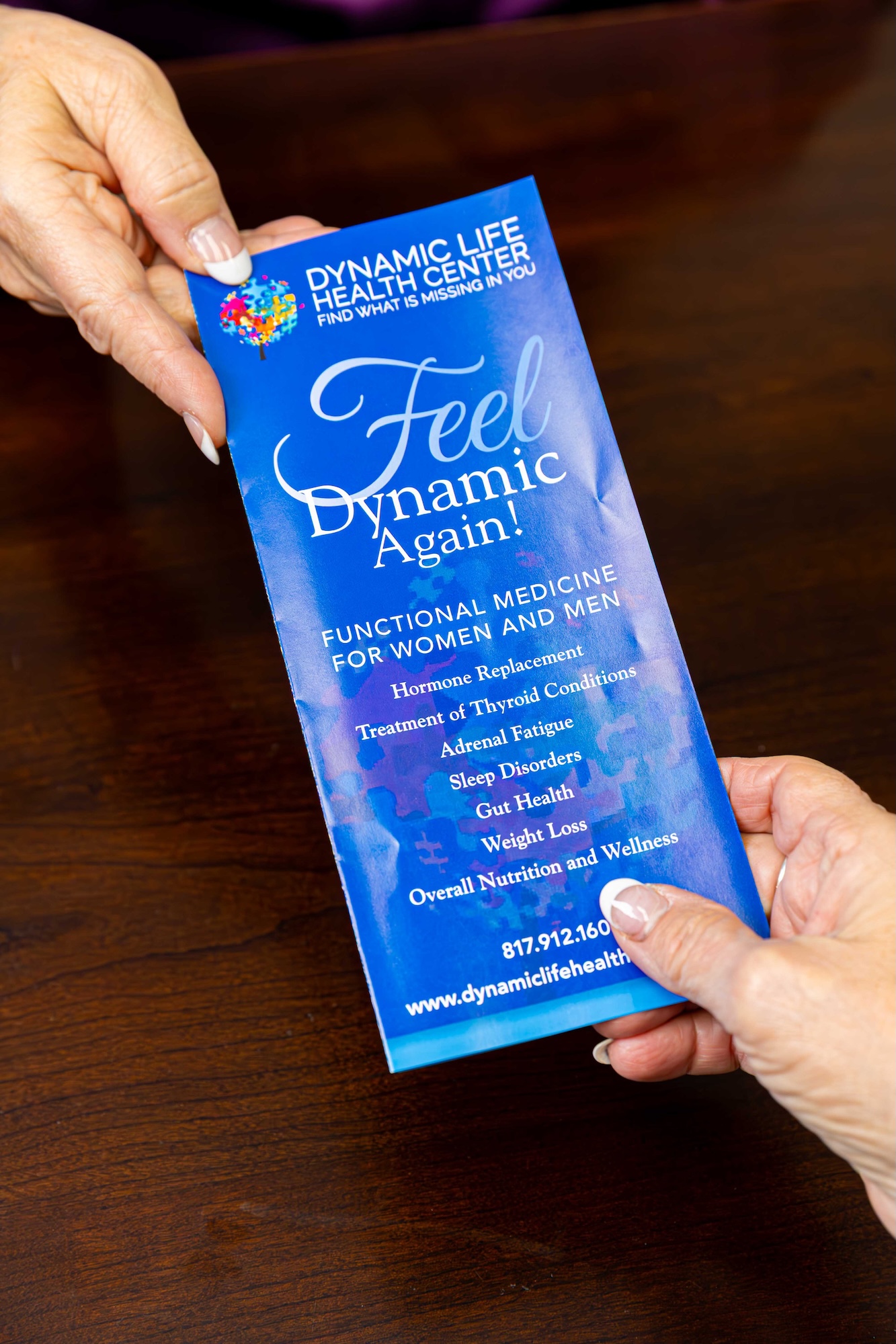 A functional Dr in Southlake hands a pamphlet on functional medicine to a patient. The blue pamphlet is visible, with information about hormone replacement, adrenal fatigue, gut health, and other disorders displayed on the front.